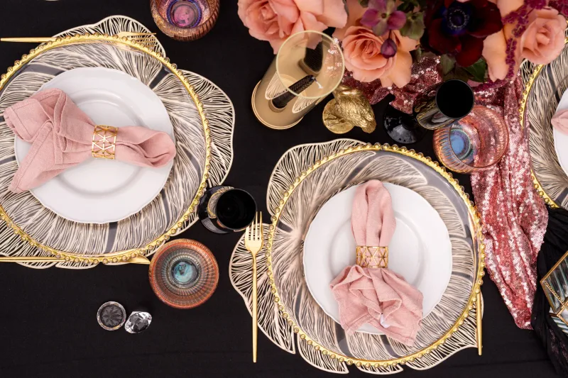 Festlich gedeckte Tafel für zwei mit goldenen Tellern, rosa Servietten und Blumenarrangement von oben