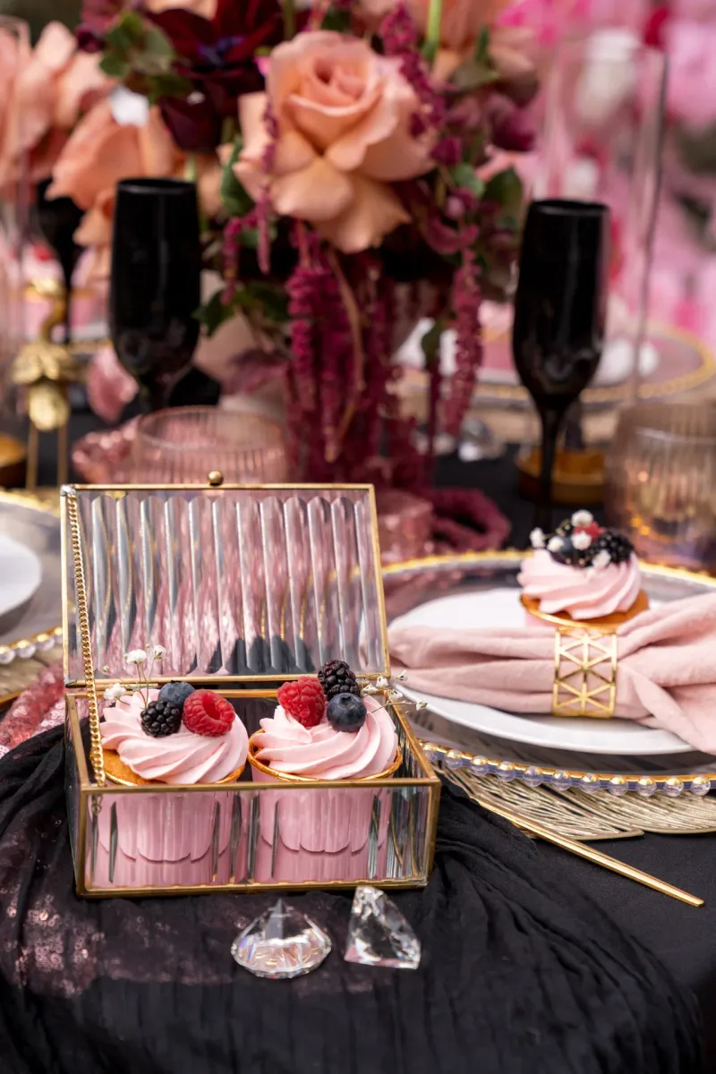 Rosafarbene Cupcakes in goldener Schmuckbox auf schwarzem Paillettentisch mit festlicher Gedeckung