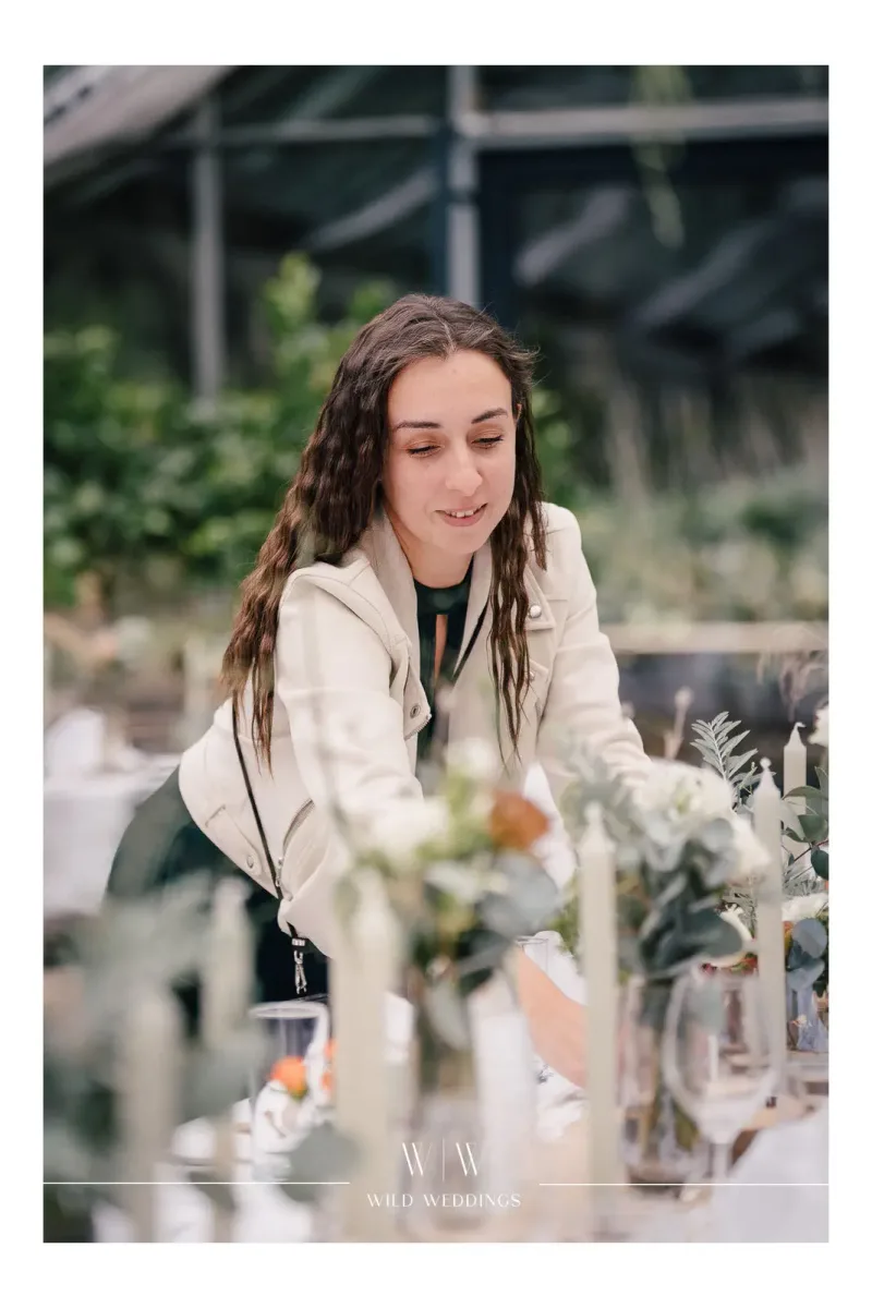 Planerin dekoriert festliche Tafel mit Kerzen und Blumenarrangement im Wintergarten