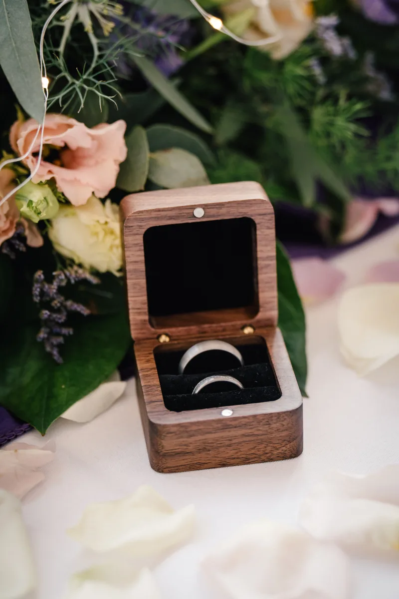 Eheringe in geöffneter Holzbox auf Blumen und Kerzen